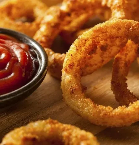 Golden-brown crispy onion rings served on wood with a side of ketchup.