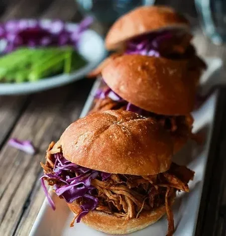 Three pulled pork sliders with purple slaw on a white dish.