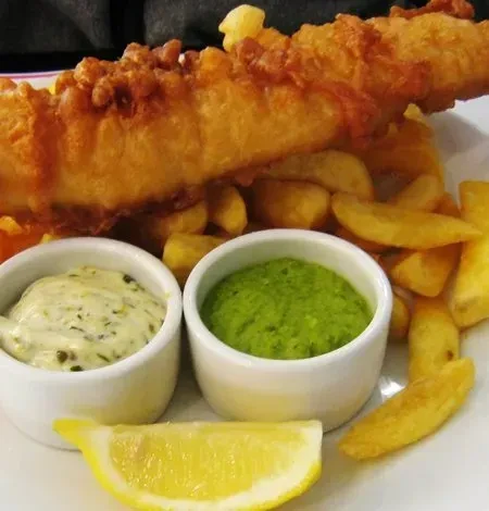 Classic fish and chips with tartar sauce, mushy peas, and lemon.