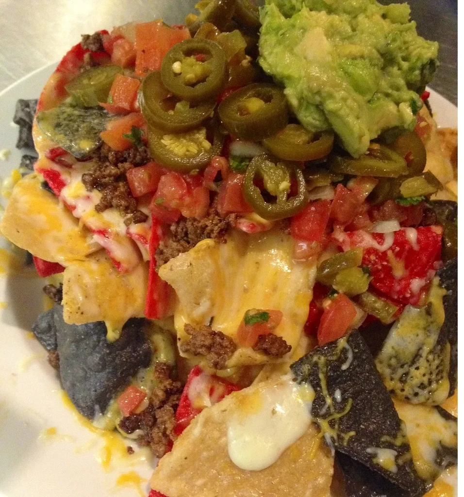Plate of loaded nachos with guacamole, jalapeños, meat, cheese, and tomatoes.