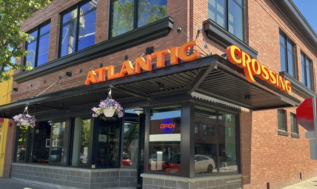 Atlantic Crossing restaurant: brick building exterior with orange sign, flowers, 'OPEN'.