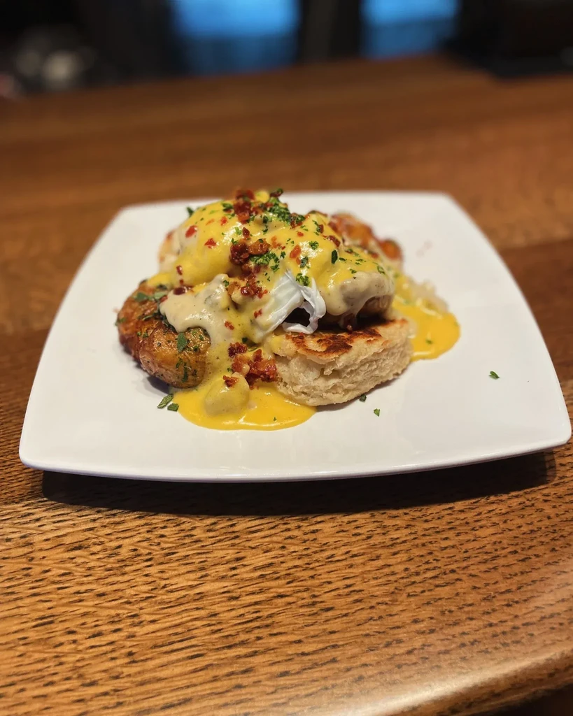 Poached eggs with hollandaise, bacon, herbs on biscuit and potato.