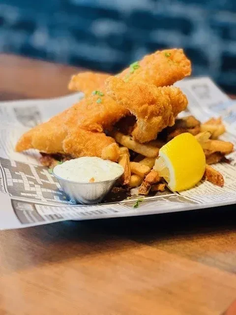 Classic fish and chips on paper with tartar sauce, lemon, and herbs.