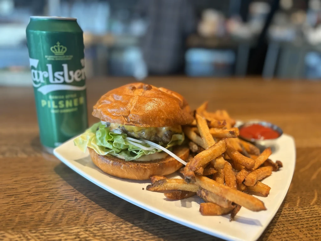 Gourmet burger, fries, ketchup, and a Carlsberg beer on a wooden table.