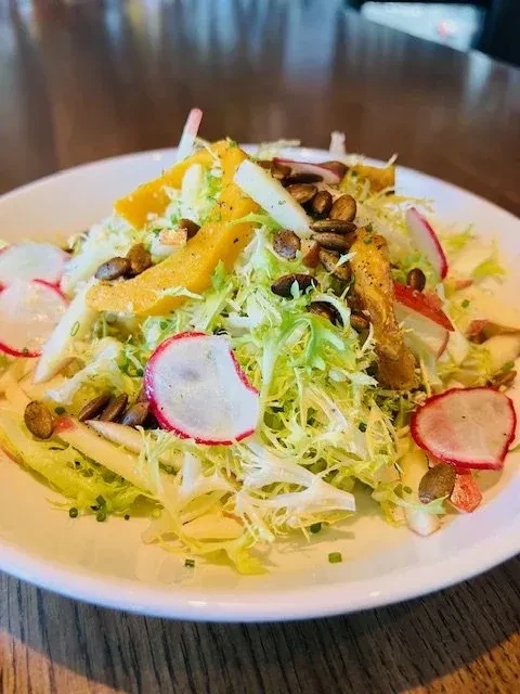 Frisée salad with orange, radishes, pumpkin seeds on a wooden table.
