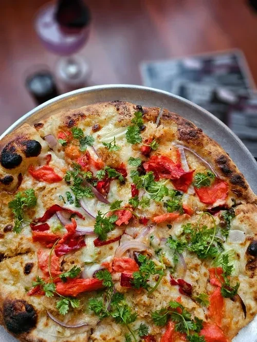 Rustic pizza with melted cheese, red peppers, onions, and fresh herbs.