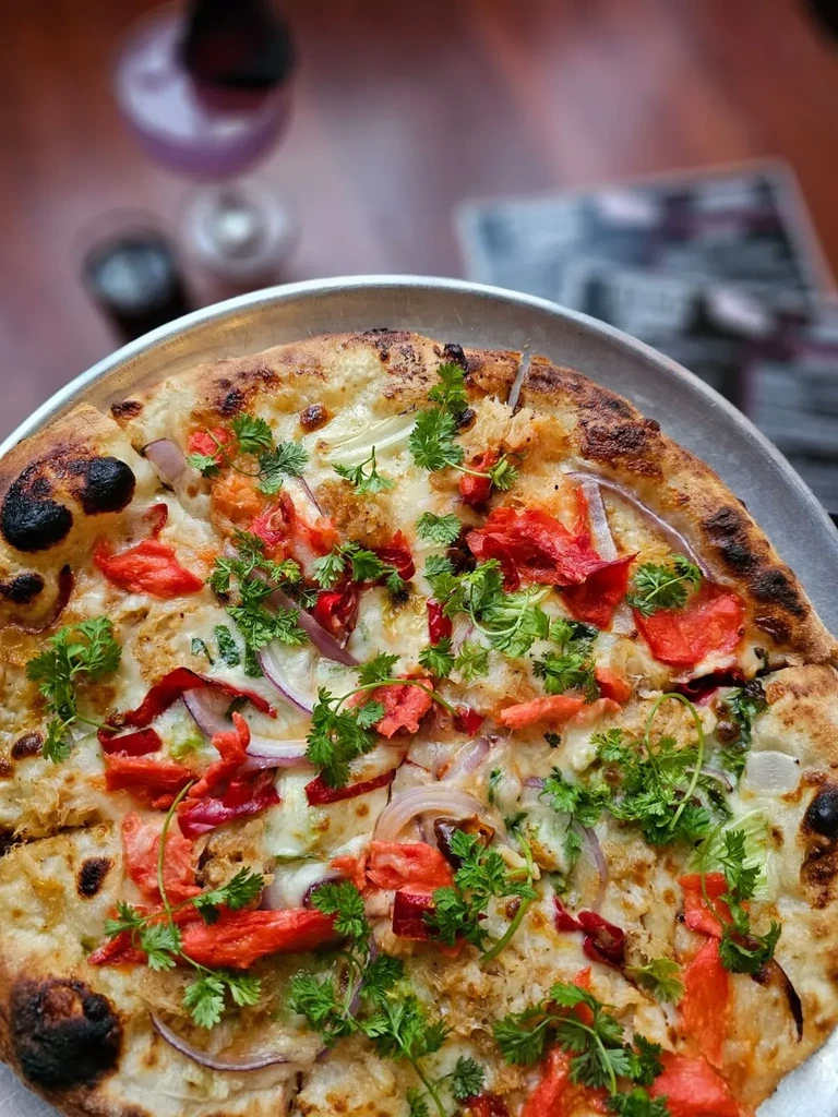 Gourmet pizza on metal pan with white base, red onions, herbs.