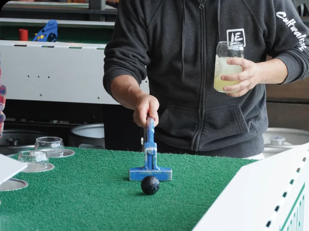 Person playing mini-golf, holding a blue putter and iced drink.