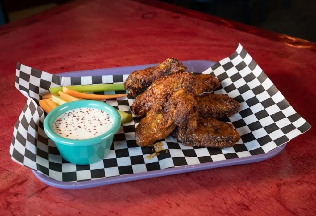 Crispy chicken wings, dipping sauce, celery, and carrots on a purple tray.