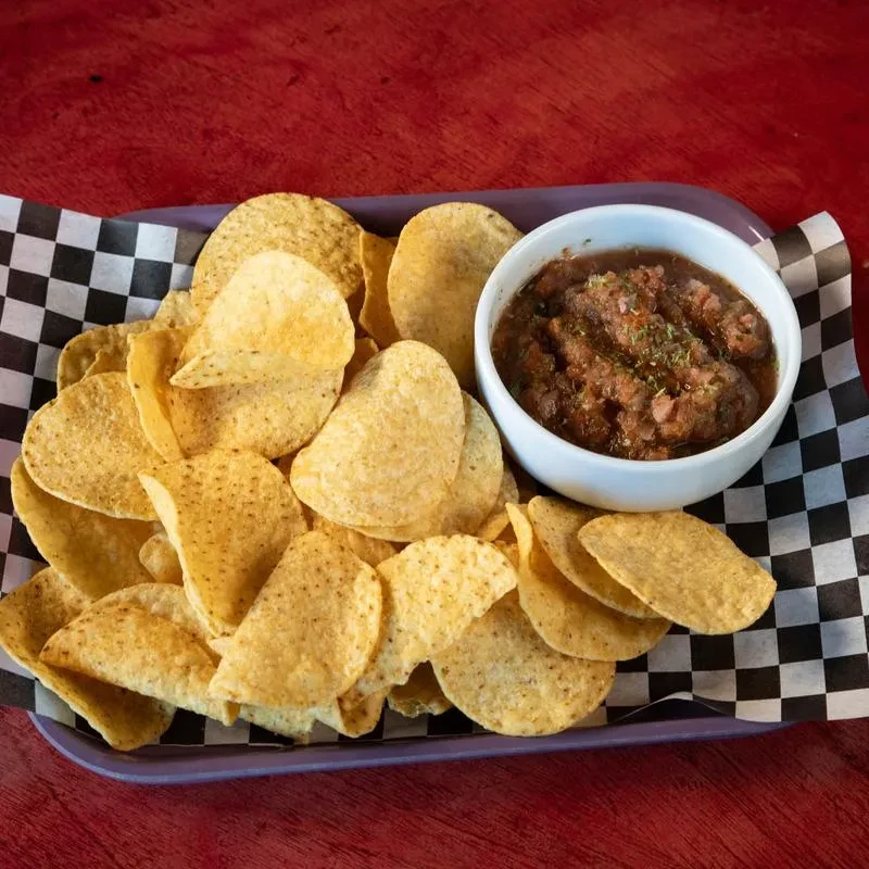 Golden tortilla chips and chunky dip on a purple checkered tray.