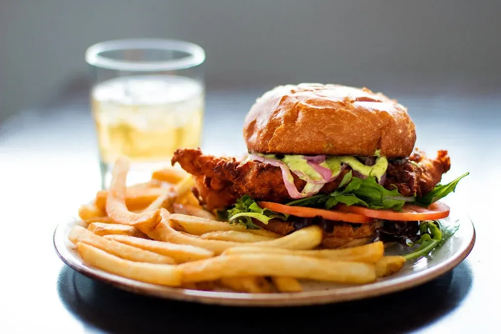 Crispy fried chicken sandwich, french fries, and drink on a white plate.