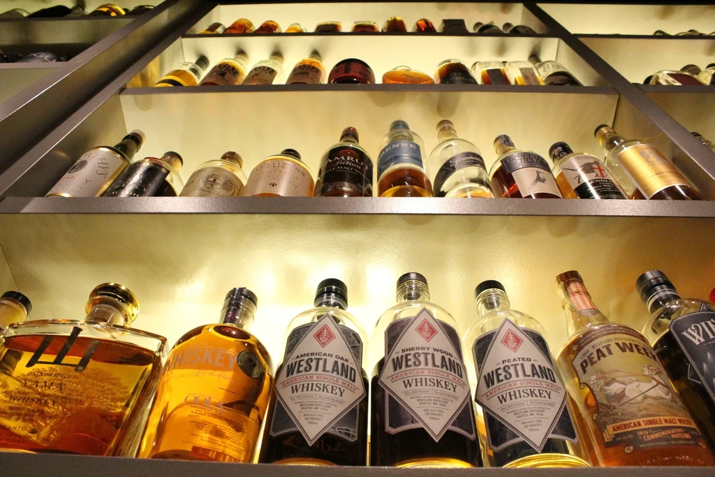 Illuminated shelves showcase various bottles of whiskey, including Westland and Peat Week.