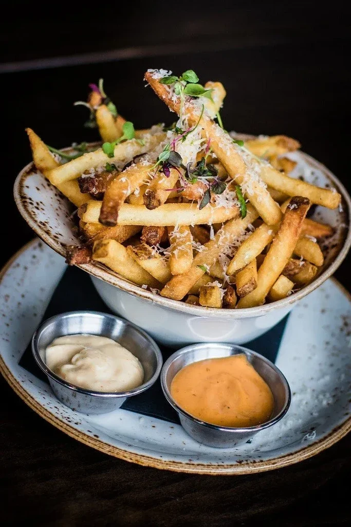 Close-up of crispy gourmet fries with Parmesan, microgreens, and two sauces.