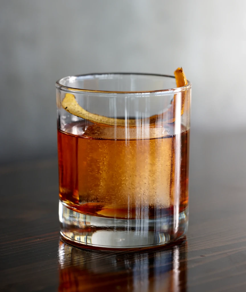Amber drink in glass tumbler with large ice and citrus peel.
