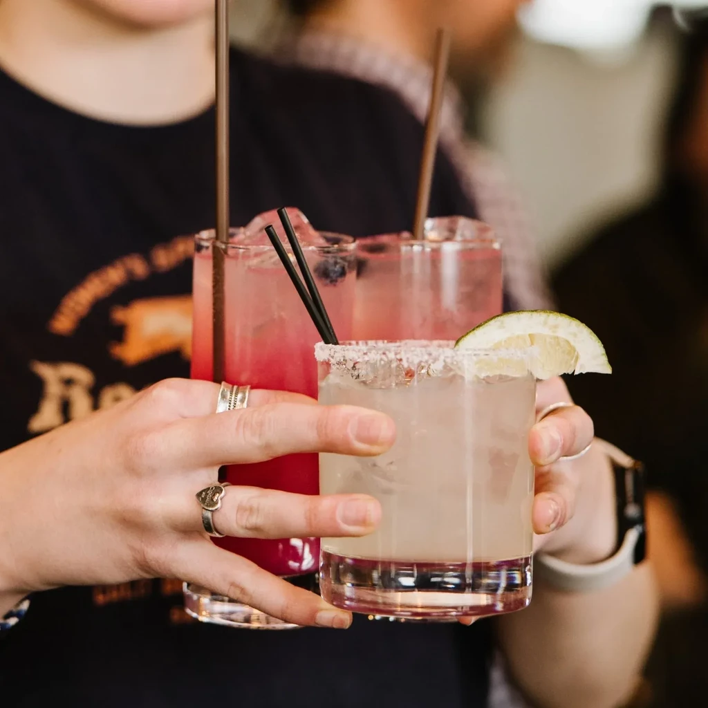 Three cocktails held by a person in a 'WOMEN'S RODEO' shirt.