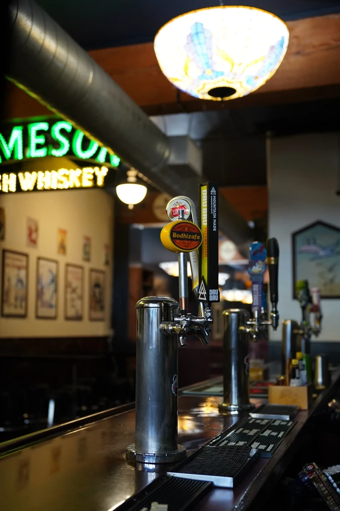 Stainless steel beer taps on a wooden bar with a Jameson sign.