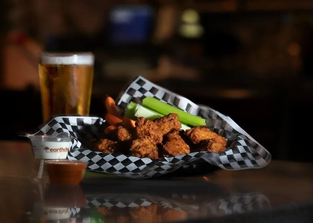 Basket of crispy golden-brown chicken wings, veggies, sauces, beer.