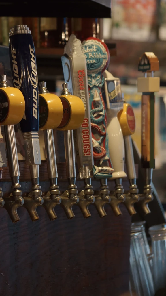 Close-up of seven diverse beer tap handles on a wooden bar.