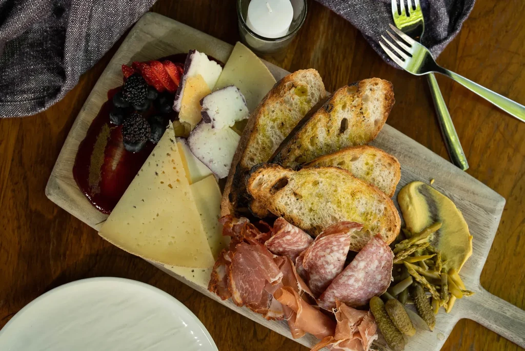 Rustic charcuterie board with sliced cheeses, meats, bread, berries, and pickles.