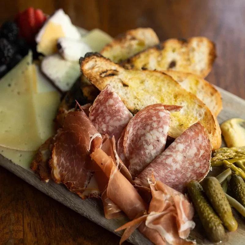 Charcuterie board with sliced meats, cheeses, bread, pickles, and berries.