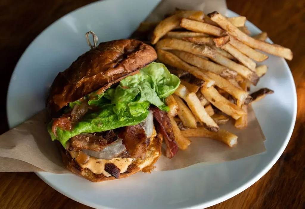 Gourmet burger with bacon, cheese, lettuce, onions, and crispy golden fries.