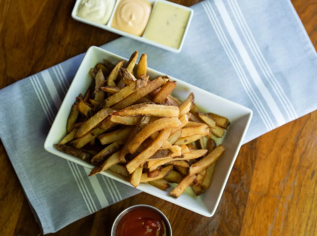 Rustic french fries with four dipping sauces on a wooden table.