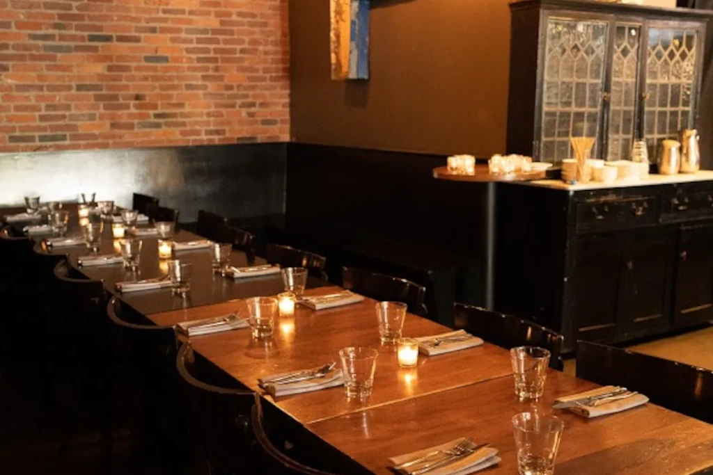Restaurant interior with serpentine wooden table, candles, and brick wall.