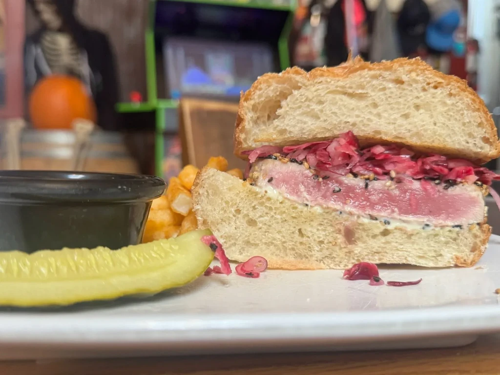 Medium-rare tuna sandwich, cut in half, with fries and a pickle.