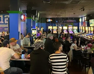 Crowded arcade bar interior featuring bright machines and blue pillars.