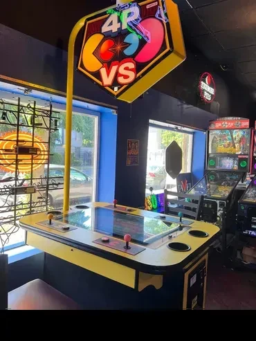Brightly lit yellow-framed 4-player Pac-Man VS arcade table in an arcade.