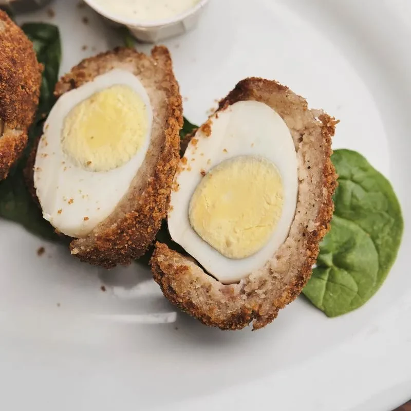 Halved Scotch egg, spinach garnish, and sauce on a white plate.