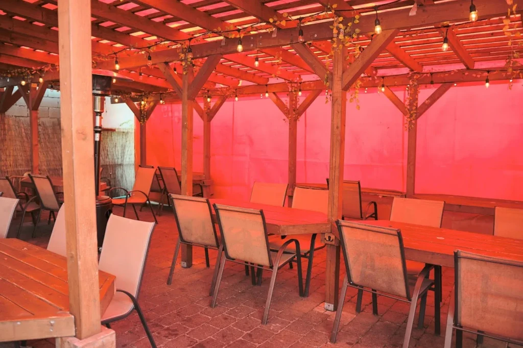 Empty restaurant patio with wooden pergola and vibrant reddish-orange light.