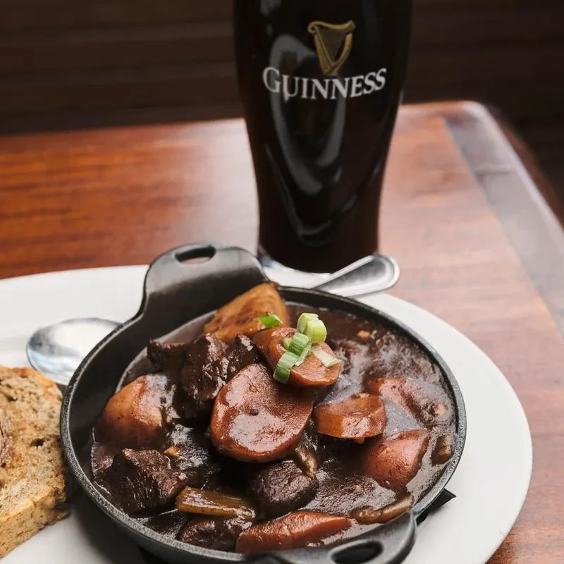 Beef stew, dark bread, and Guinness pint on a rustic wooden table.