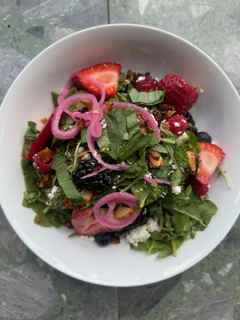 Colorful berry salad with greens, pickled onion, and crumbled cheese.