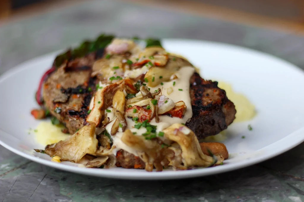 Grilled meat with creamy mushroom sauce, potato purée, and chives.