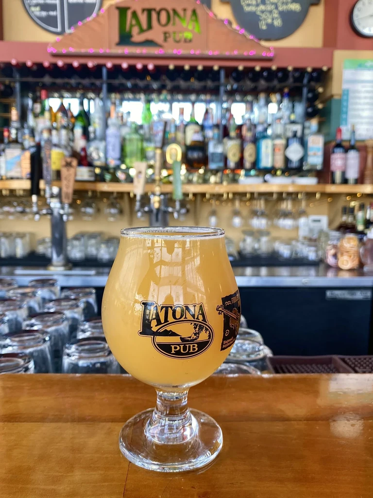 Hazy beer in a branded Latona Pub glass on a bar.