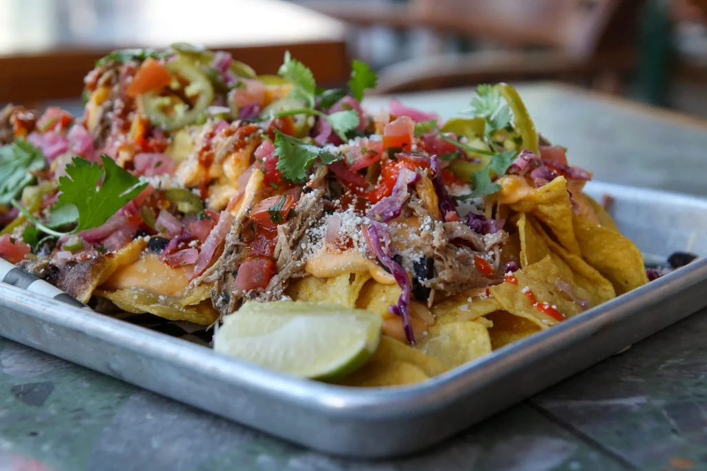 Fully loaded nachos on metal tray with cheese, meat, veggies, lime.