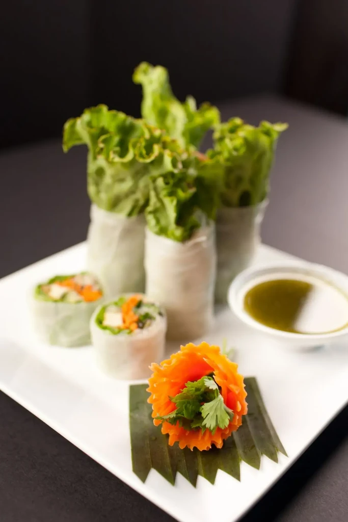 Platter of fresh spring rolls, cut sections, dipping sauce, and carved carrot.