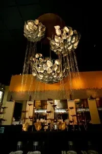 Three sparkling metallic leaf chandeliers in a dim restaurant or bar.