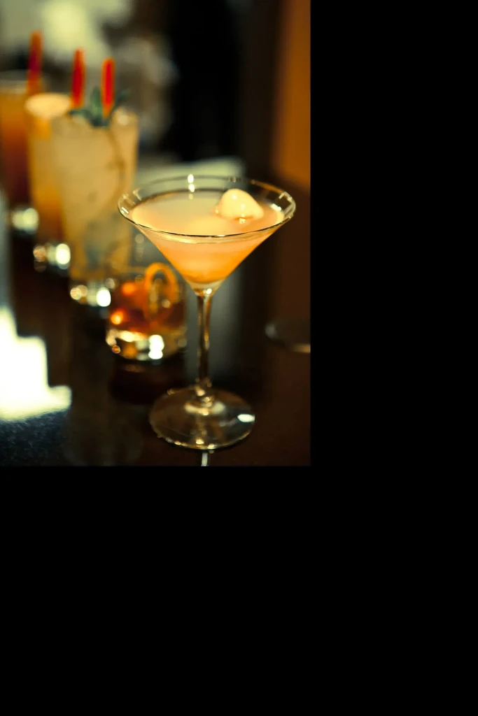 Close-up of several cocktails on a dim, reflective bar. Martini in front.