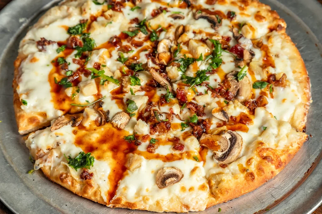 Overhead pizza with chicken, mushrooms, bacon, melted cheese, sauce, and herbs.