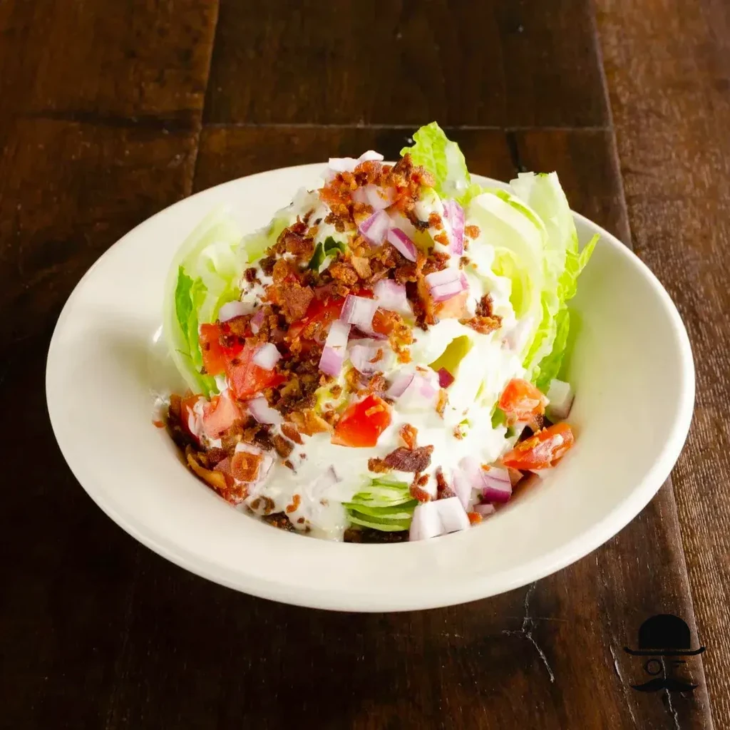 Wedge salad topped with bacon, tomatoes, onions, and creamy dressing.