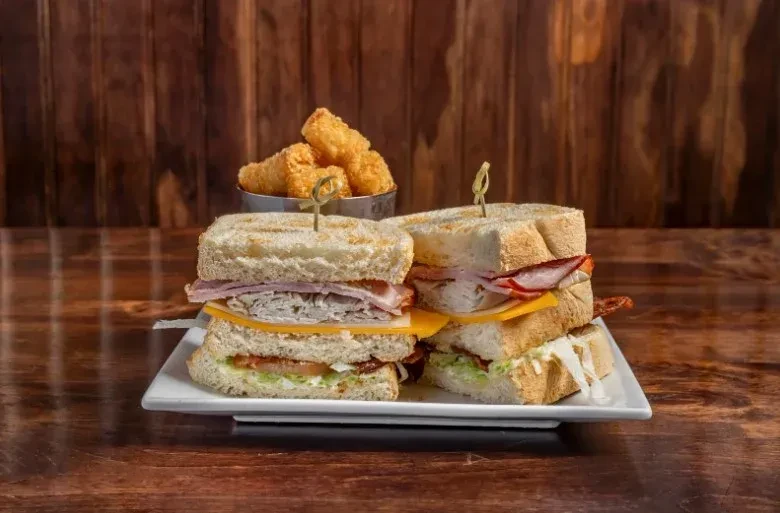Two multi-layered club sandwiches with meat, cheese, bacon, and fries.