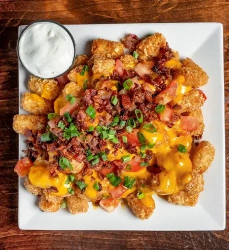 Loaded tater tots with melted cheese, bacon, tomatoes, and a dipping sauce.