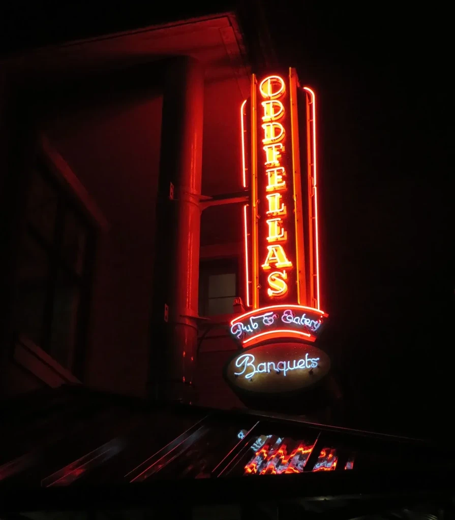 Vertical neon sign for ODDELLAS Pub & Eatery, Banquets, at night.