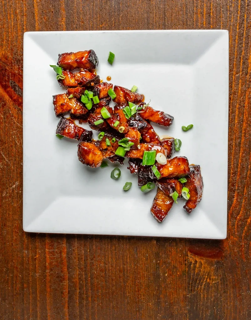 Overhead shot of glazed meat with green onions on a white plate.