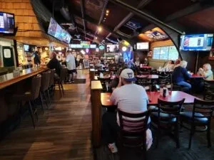 Dimly lit sports bar interior with a long bar, TVs, and patrons.