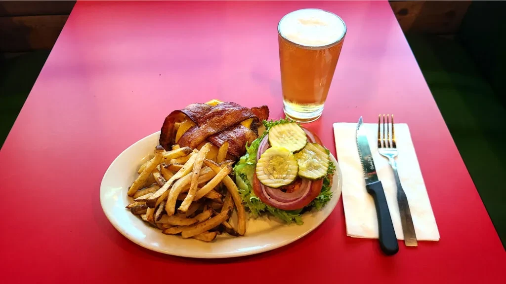 Bacon burger, fries, loaded bun, and beer on a red table.