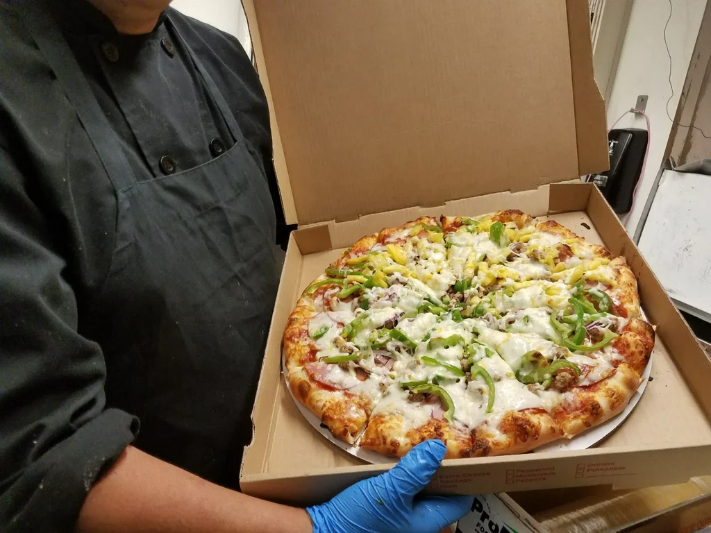 Freshly baked pizza with diverse toppings held by a chef in a box.