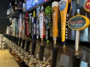 Close-up of diverse branded beer tap handles at a bar.